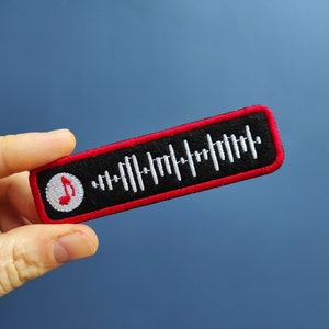Pode incluir: Um remendo bordado vermelho e preto com uma nota musical branca e um padrão semelhante a um código de barras branco. O texto "Spotify" não é visível na imagem.