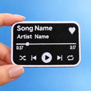 Może przedstawiać: Prostokątna, czarna haftowana naszywka z białymi przeszyciami, przedstawiająca interfejs odtwarzacza muzyki. Zawiera tekst Song Name i Artist Name, ikonę serca, pasek postępu, czasy 0:37 i 3:17 oraz przyciski sterowania odtwarzaniem.