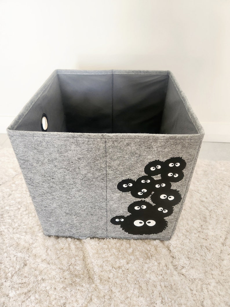 May include: A gray felt storage bin with a black and white graphic of a cartoon character with multiple eyes. The bin has a round hole on the side.