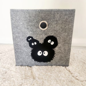May include: A gray felt storage bin with a black and white graphic of a cartoon character with large eyes. The bin has a black metal handle.