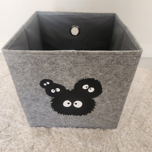 May include: A gray felt storage bin with a black and white graphic of a cartoon character with multiple eyes. The bin has a round hole in the top.