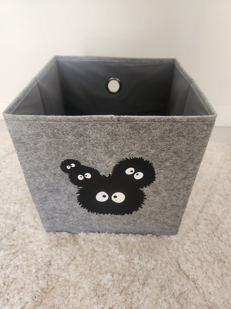 May include: A gray felt storage bin with a black and white graphic of a cartoon character with multiple eyes. The bin has a round hole in the top.