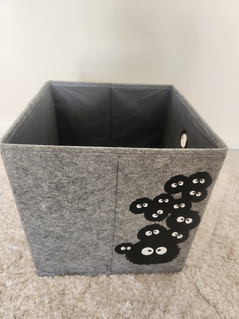 May include: A gray felt storage box with a black and white graphic of a group of Totoro characters. The box has a round hole on the side.