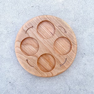 Peut inclure: Un plateau de service rond en bois avec quatre indentations circulaires et des fl&egrave;ches grav&eacute;es dans le bois. Le plateau est en bois brun clair.