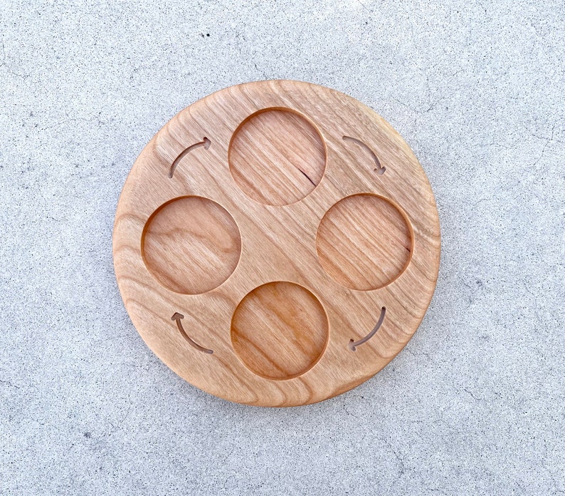 Peut inclure: Un plateau de service rond en bois avec quatre indentations circulaires et des fl&egrave;ches grav&eacute;es dans le bois. Le plateau est en bois brun clair.