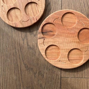 Peut inclure: Un plateau de service en bois avec six indentations circulaires, chacune avec une fl&egrave;che sculpt&eacute;e dans le bois. Le plateau est en bois brun clair avec une finition naturelle.