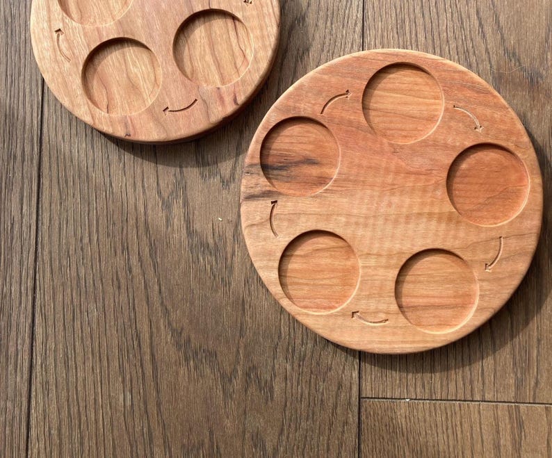 Peut inclure: Un plateau de service en bois avec six indentations circulaires, chacune avec une fl&egrave;che sculpt&eacute;e dans le bois. Le plateau est en bois brun clair avec une finition naturelle.