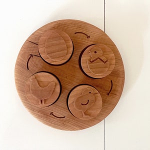 Peut inclure: Puzzle circulaire en bois compos&eacute; de quatre pi&egrave;ces. Les pi&egrave;ces repr&eacute;sentent un poussin &eacute;closant d'un &oelig;uf, un poussin et un &oelig;uf. Le puzzle est en bois brun clair.