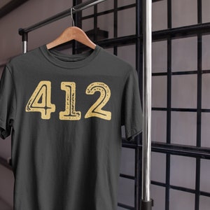 May include: A dark grey t-shirt with a yellow distressed graphic of the number 412.