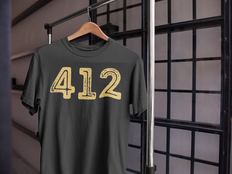 May include: A dark grey t-shirt with a yellow distressed graphic of the number 412.