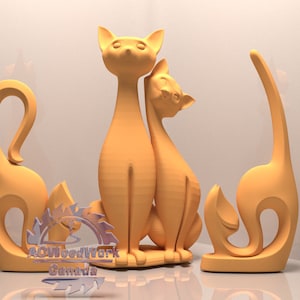 Op de afbeelding: Drie houten kattenbeeldjes in een licht oranje kleur. De beeldjes zijn gestileerd en abstract, met de lichamen en staarten van de katten die een continue curve vormen. De beeldjes zijn in een driehoekige formatie geplaatst, met de twee grotere katten in het midden en de kleinere kat links.