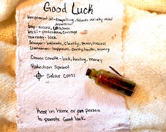 May include: A handwritten list of ingredients and their associated benefits for good luck, including bergamot oil, bay leaves, basil, nutmeg, ginger, cinnamon, and a green candle. The list also includes a protection symbol, a solar cross, and a small bottle of oil. The text reads "Good Luck" and "Keep in home or on person to promote good luck."