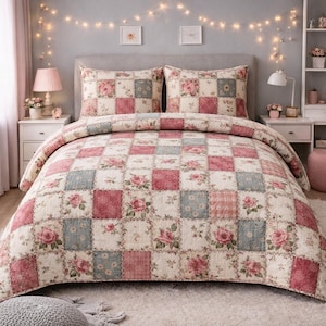 May include: A bed dressed with a patchwork quilt and two pillowcases. The quilt has a pattern of cream, pink, and blue squares, decorated with floral and rose motifs. The bed is set against a neutral headboard and bedside tables.