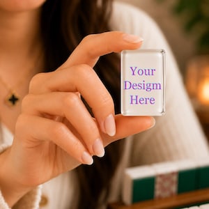 Puede incluir: Una ficha rectangular de acr&iacute;lico transparente con esquinas redondeadas que presenta el texto morado Your Design Here impreso en la superficie frontal. La ficha se sostiene en posici&oacute;n vertical, mostrando su acabado liso.