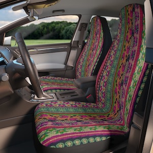 Puede incluir: Fundas de asiento de coche con un diseño colorido y estampado. Las fundas presentan una mezcla de rayas y formas geométricas rosas, verdes, naranjas y moradas. El interior del coche incluye un volante y una vista de un campo verde.