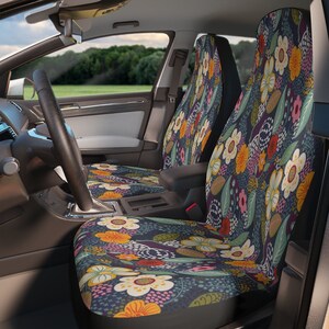 Puede incluir: Fundas de asiento de coche con un estampado floral. Las fundas presentan un fondo azul oscuro con un diseño repetido de flores blancas, amarillas, naranjas y rosas, junto con hojas verdes y moradas. Se ve el interior de un coche.