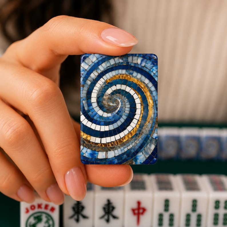 May include: A rectangular mahjong tile featuring a mosaic-style design with a swirling pattern of blue, white, and gold tiles. The surface is composed of small, square-shaped segments arranged in a spiral, creating a textured, multi-colored visual effect.