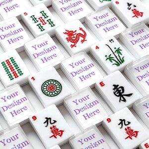 Puede incluir: Una colecci&oacute;n de fichas de mahjong rectangulares blancas dispuestas en una cuadr&iacute;cula. Algunas fichas presentan s&iacute;mbolos tradicionales rojos, verdes y negros, incluyendo un drag&oacute;n, bamb&uacute; y caracteres chinos. Otras fichas muestran el texto Your Design Here.