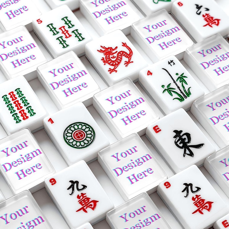 Puede incluir: Una colecci&oacute;n de fichas de mahjong rectangulares blancas dispuestas en una cuadr&iacute;cula. Algunas fichas presentan s&iacute;mbolos tradicionales rojos, verdes y negros, incluyendo un drag&oacute;n, bamb&uacute; y caracteres chinos. Otras fichas muestran el texto Your Design Here.