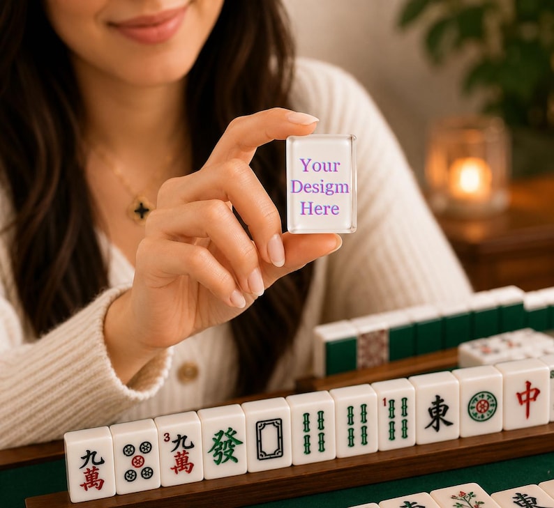 Puede incluir: Una ficha de mahjong rectangular blanca con un frente de acr&iacute;lico transparente que presenta el texto morado Your Design Here. La ficha se sostiene en posici&oacute;n vertical, mostrando una superficie lisa y bordes limpios, junto a otras fichas en un soporte.
