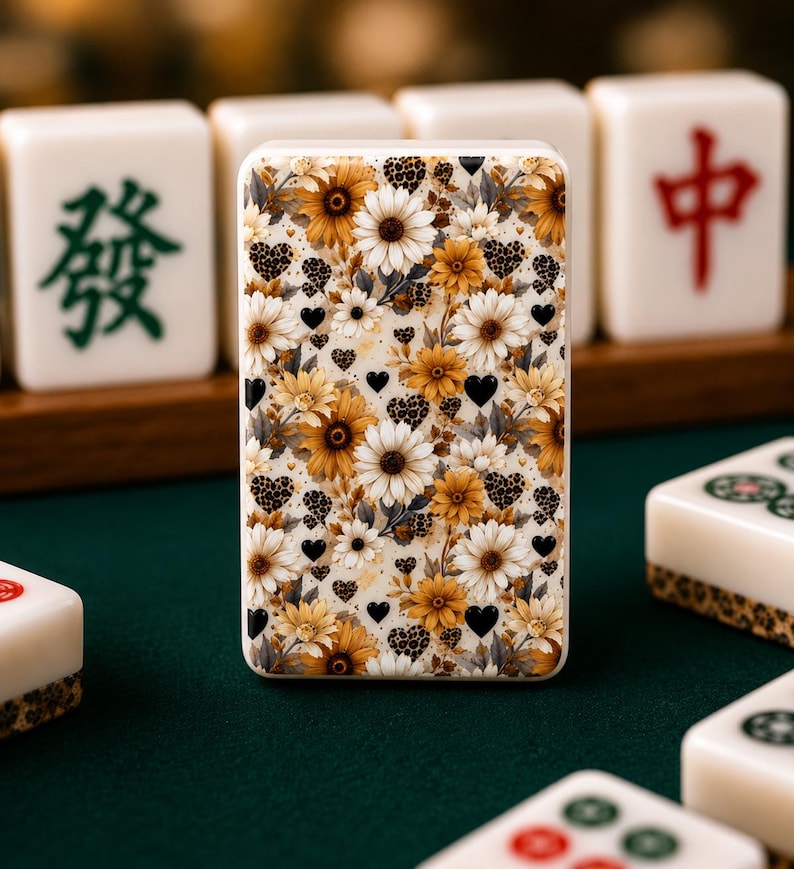 May include: A rectangular phone case featuring a floral design with yellow and white daisies, leopard print hearts, and black hearts. The case is surrounded by white Mahjong tiles with green and red Chinese characters.