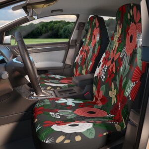 May include: Two car seat covers with a floral pattern. The covers are black with red, white, and green flowers. The flowers are stylized and have a modern look.