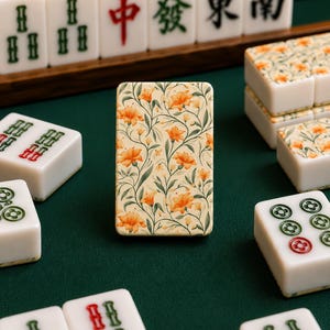May include: A single mahjong tile standing upright in the center, featuring a cream background with a repeating pattern of orange flowers and green stems. Surrounding it are various standard white mahjong tiles with green and red character markings.