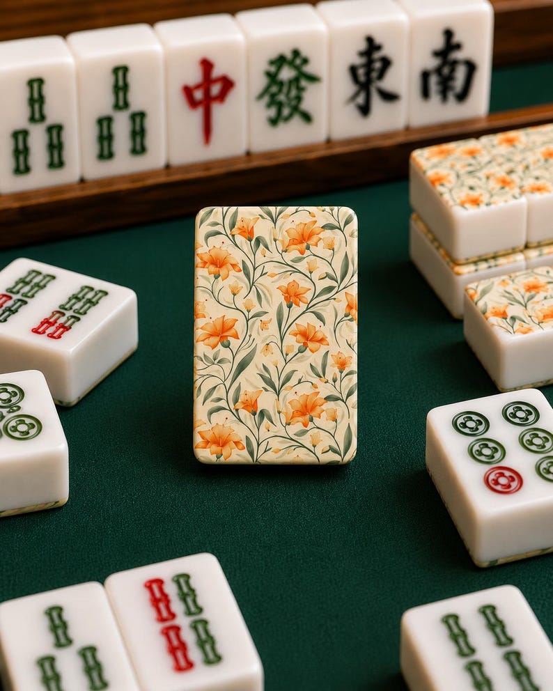 May include: A single mahjong tile standing upright in the center, featuring a cream background with a repeating pattern of orange flowers and green stems. Surrounding it are various standard white mahjong tiles with green and red character markings.