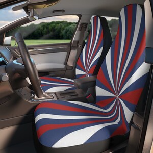 Puede incluir: Fundas de asiento de coche con un diseño en espiral rojo, blanco y azul. El patrón irradia desde un punto central, creando un efecto dinámico y llamativo. Las fundas están instaladas en el interior de un coche, con vista al volante y al paisaje exterior.