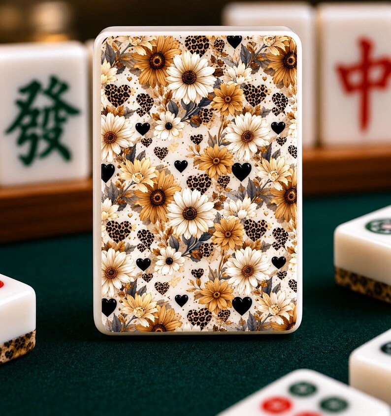 May include: A rectangular Mahjong tile with a floral design featuring sunflowers, white daisies, and black heart accents. The tile has a cream-colored background with leopard print details. Other Mahjong tiles are visible in the background.