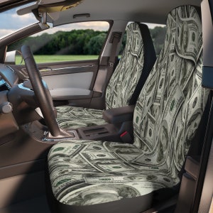 Puede incluir: Dos fundas para asientos de coche con un patrón de billetes de dólar estadounidense. Las fundas de los asientos son negras con un patrón de billetes de dólar verde y blanco.