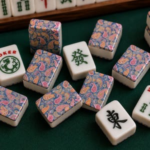 May include: A set of mahjong tiles featuring a mix of white tiles with green or black Chinese characters and tiles with a colorful blue, pink, and orange paisley pattern. One tile displays the word JOKER above a green dragon illustration.