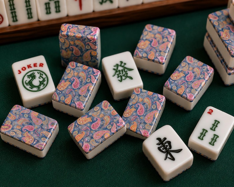 May include: A set of mahjong tiles featuring a mix of white tiles with green or black Chinese characters and tiles with a colorful blue, pink, and orange paisley pattern. One tile displays the word JOKER above a green dragon illustration.