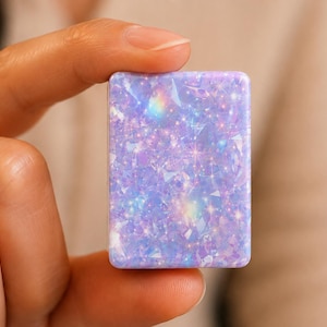 May include: A rectangular, flat object featuring a vibrant lavender and light blue surface with a dense, shimmering holographic pattern of geometric shards and small, bright star-like sparkles that create a multi-dimensional, reflective effect.
