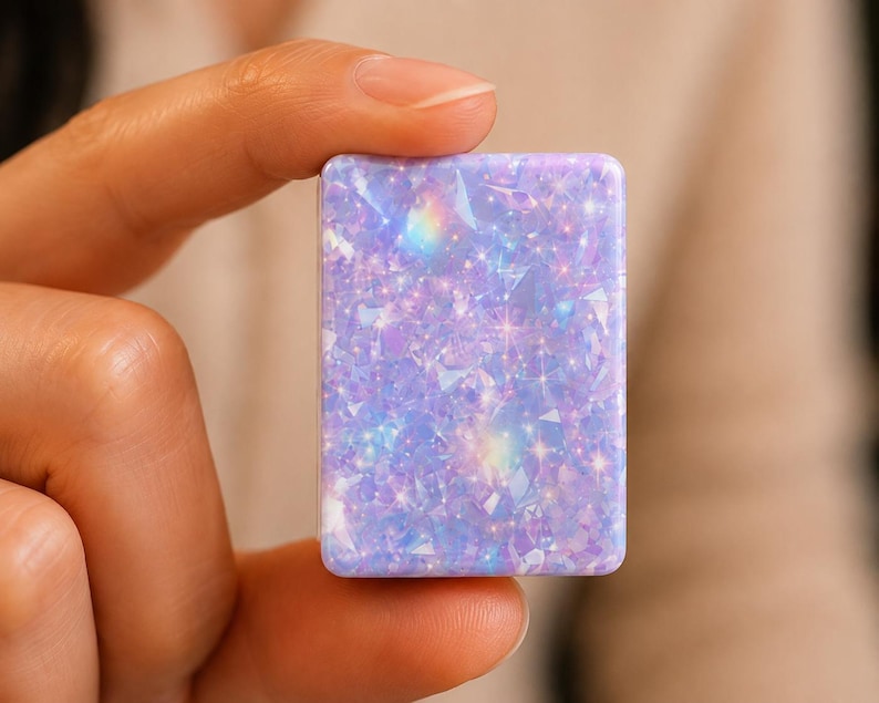 May include: A rectangular, flat object featuring a vibrant lavender and light blue surface with a dense, shimmering holographic pattern of geometric shards and small, bright star-like sparkles that create a multi-dimensional, reflective effect.
