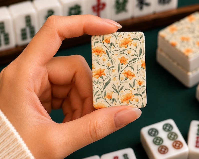 May include: A rectangular mahjong tile featuring a cream-colored background decorated with a repeating pattern of orange flowers and green stems. The tile has rounded corners and a smooth finish, displaying a botanical design on its front surface.