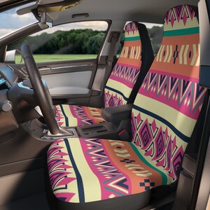Puede incluir: Fundas de asiento de coche con un colorido estampado geométrico en tonos rosa, naranja, turquesa y crema. Las fundas están instaladas en un coche, con el volante y el salpicadero visibles. El diseño tiene una estética del suroeste o tribal.