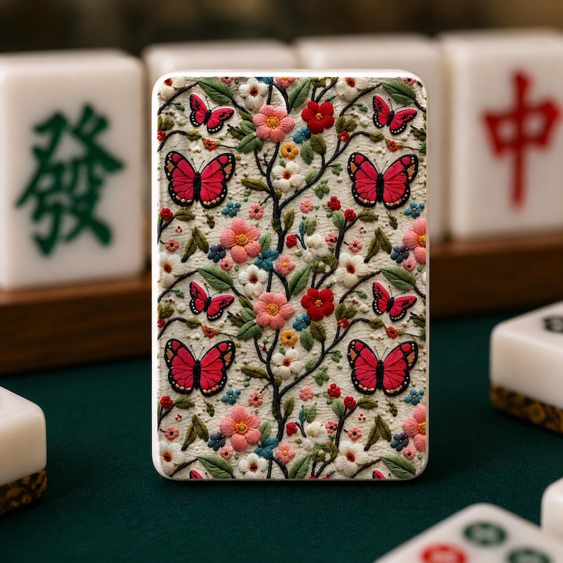May include: A rectangular Mahjong tile with a detailed floral and butterfly design. The design features red butterflies, pink, red, and white flowers, and green leaves on a cream background. Other Mahjong tiles are visible in the background.