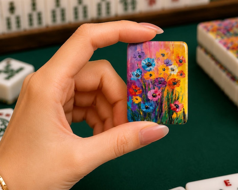 May include: A rectangular mahjong tile featuring a vibrant, multi-colored floral painting. The artwork displays a dense cluster of stylized flowers in shades of blue, yellow, red, purple, and pink against a bright yellow and green background.