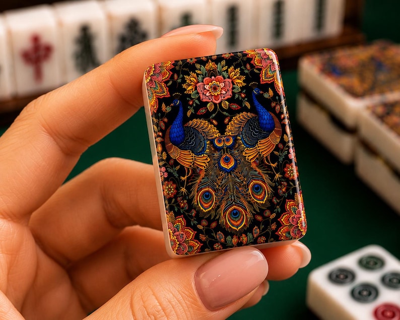 Puede incluir: Una ficha de mahjong rectangular que presenta una ilustraci&oacute;n detallada y colorida de dos pavos reales con plumaje azul y dorado vibrante, rodeados de intrincados patrones florales sobre un fondo negro, con base blanca y bordes redondeados.