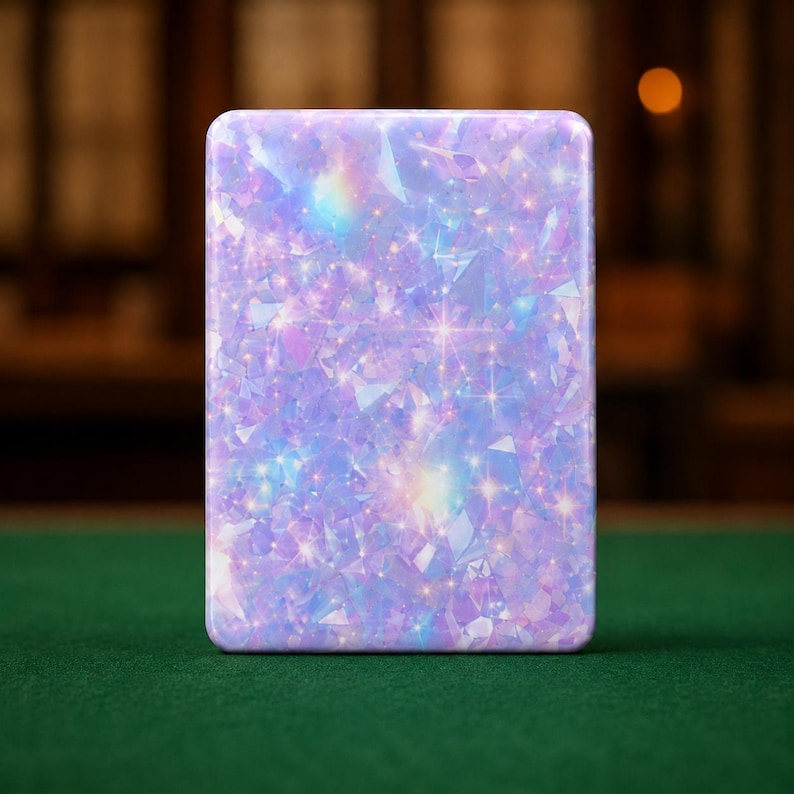 May include: A rectangular metal tin featuring a vibrant, iridescent pattern of light purple, blue, and pink crystalline shapes. The surface displays a shimmering, holographic effect with numerous small, bright star-like sparkles scattered throughout.
