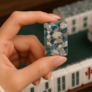 May include: A rectangular mahjong tile featuring a mosaic pattern of blue, white, and gray stone-like fragments held together by thin gold-colored lines. The tile has a smooth, polished surface and rounded corners, matching other tiles in the set.