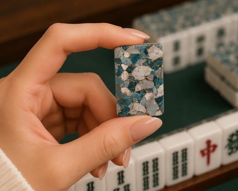 May include: A rectangular mahjong tile featuring a mosaic pattern of blue, white, and gray stone-like fragments held together by thin gold-colored lines. The tile has a smooth, polished surface and rounded corners, matching other tiles in the set.