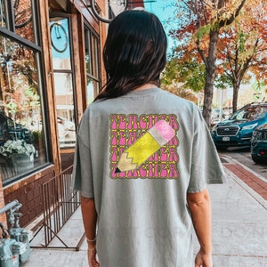 May include: A gray oversized t-shirt with a graphic of a yellow pencil and the word "TEACHER" repeated in a retro font.