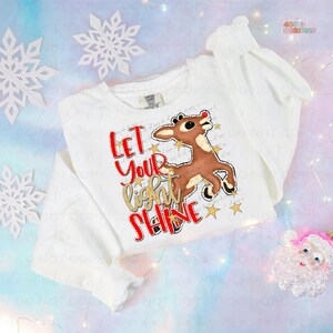 May include: White sweatshirt with a red and brown reindeer illustration and gold glitter text that reads "Let your light shine".
