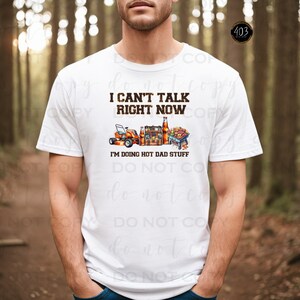 May include: White t-shirt with the text "I can't talk right now I'm doing hot dad stuff" and a graphic of a lawnmower, beer, and a grill.