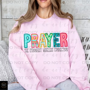 May include: Pink sweatshirt with the text "PRAYER" in colorful patchwork letters and the text "The Strongest Wireless Connection" below.