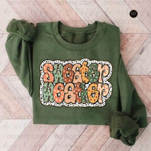 May include: A green sweatshirt with a colorful "Sweater Weather" graphic featuring polka dots. The graphic is in a retro style with a white outline.