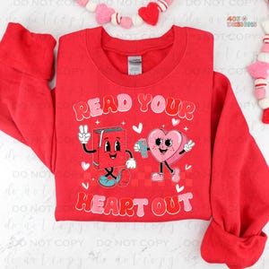 May include: Red sweatshirt with a graphic of a book and a heart holding hands. The text "Read Your Heart Out" is printed on the sweatshirt.