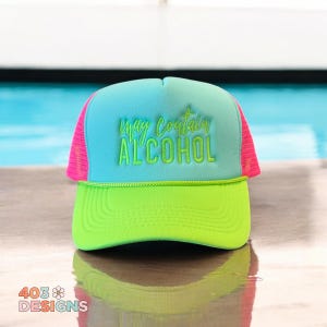 May include: A neon green and blue trucker hat with the text "may contain ALCOHOL" in green. The hat has a pink mesh back and a green brim. The hat is sitting on a wooden surface.